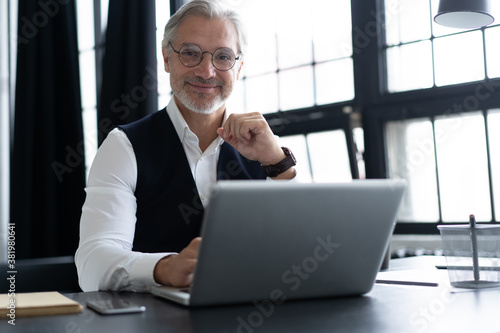 Concentrated at work. Happy mature man in full suit using laptop while working in modern office