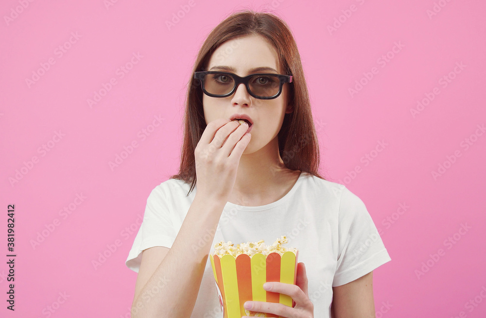 Front view of impassive female model in glasses eating popcorn looking at camera isolated on pink Front view of impassive female model in glasses eating popcorn looking at camera isolated on pink