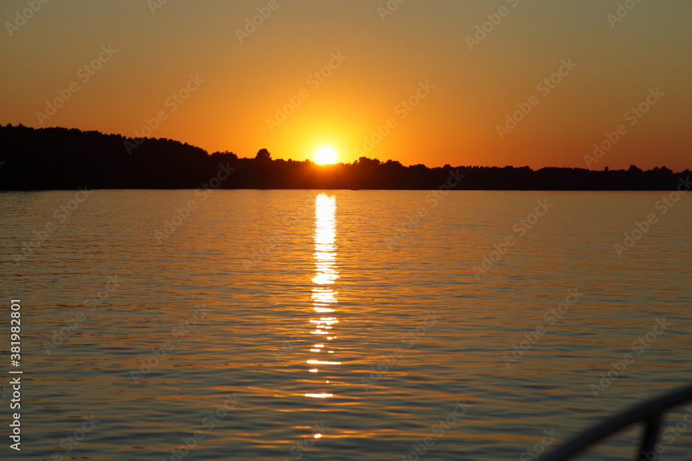 Beautiful sunset, bright orange sunshine with reflection track in calm water on forest on Horizon background at Sunny summer evening, tranquilty relax photo  picture, view from yacht deck railing
