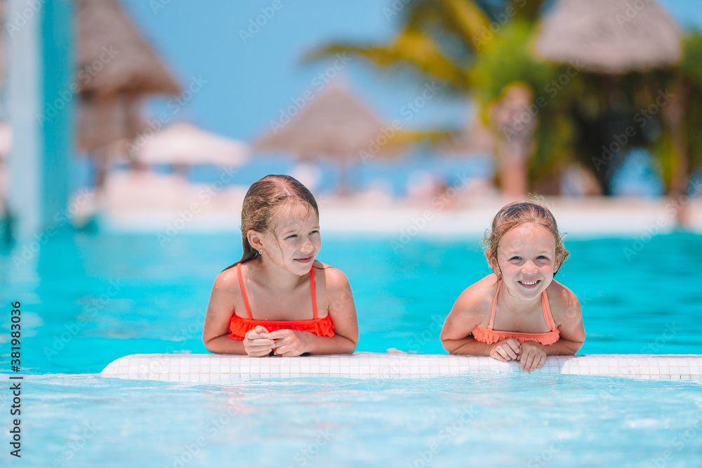 Adorable little girls playing in outdoor swimming pool on vacation
