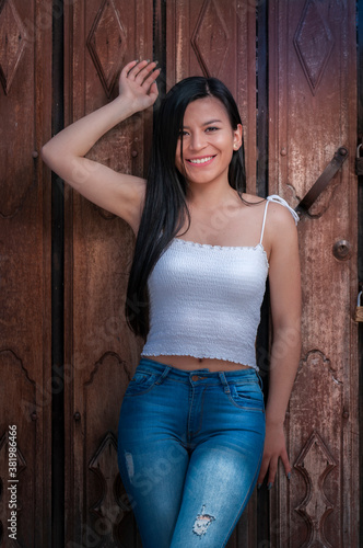 happy hispanic woman with long, black, smiling hair leaning against a wooden door