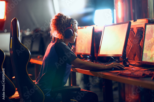 Cybersport concept. Side view of a focused teenage girl, professional gamer wearing headphones participating in eSport tournament photo