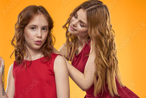 A red-haired girl and a beautiful woman on a yellow background in red dresses gesticulate with their hands and grimace