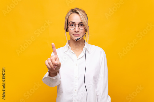 young woman telemarketer smiling and looking friendly, showing number one or first with hand forward, counting down photo