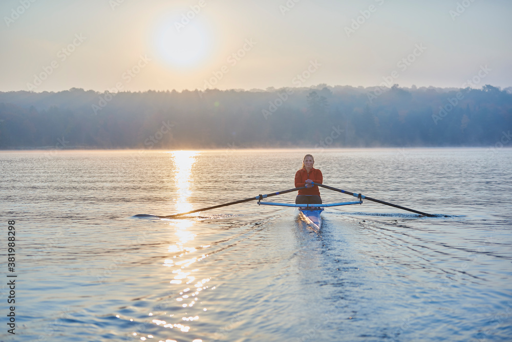 Middle aged woman rowing on calm autumn lake at early morning with mist over water. Middle aged woman rowing on calm autumn lake at early morning with mist over water.