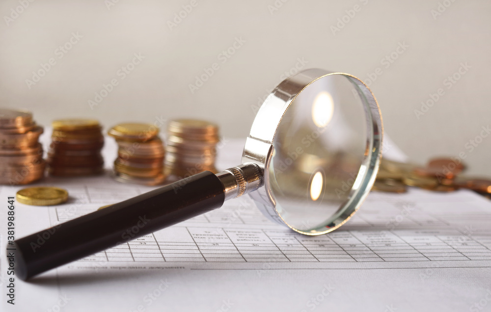 Magnifying glass and coins on financial documents, accounting background. Financial and economic concept. Magnifying glass and coins on financial documents, accounting background. Financial and economic concept.
