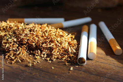 Fotografie a pile of dried tobacco and cigarettes lies on a brown wooden table, lit by the