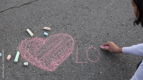 A woman drawing a heart and word LOVE with a chalk on asphalt. Drawings paintings on asphalt
