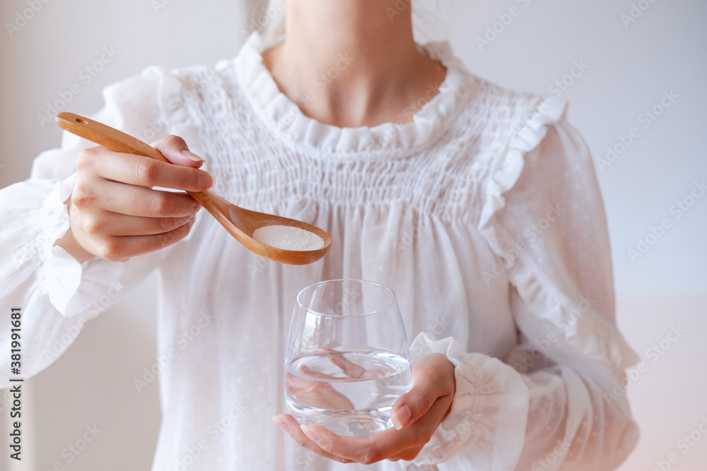 Woman in white blouse holding wooden spoon with magnesium or calcium supplement powder and water glass. Bioactive additive woman pharmacy. Vitamin mineral treatment. Infant formula. Protein powder. - obrazy, fototapety, plakaty 