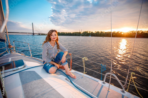 a girl in jeans sits on a yacht and looks at the sunset