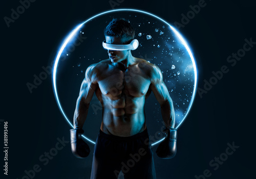 Muscular model sports young man in glasses of virtual reality and boxing gloves on dark background. Fashion portrait of strong brutal guy. Sexy torso. Male flexing his muscles. VR. Blue neon light.