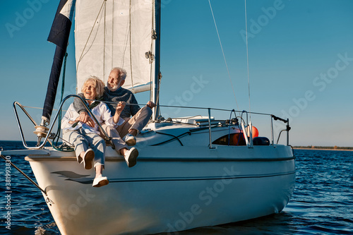 Sea trip. Happy beautiful senior family couple hugging and having fun while relaxing on a sail boat or yacht deck floating in a calm blue sea, they enjoying amazing sunset