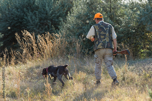 Duck hunter with shotgun walking through a meadow. .Rear view of a man with a weapon in his hands.