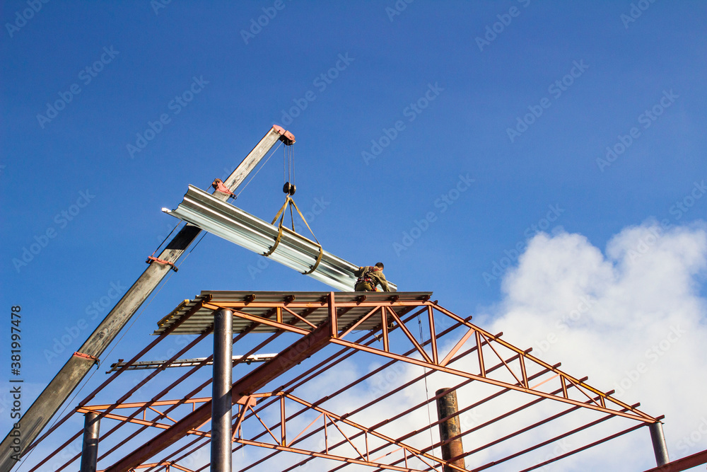 Mobile crane lifting metal roof sheet on palate truss up to stock above