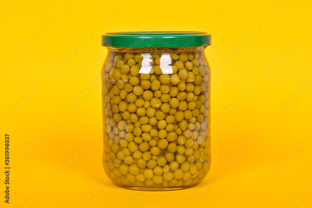 Canned green peas in a glass jar on a yellow background. Canned green peas in a glass jar on a yellow background.