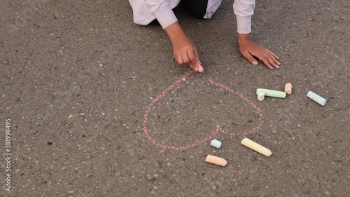 A woman drawing a heart with a chalk on asphalt. Drawings paintings on asphalt