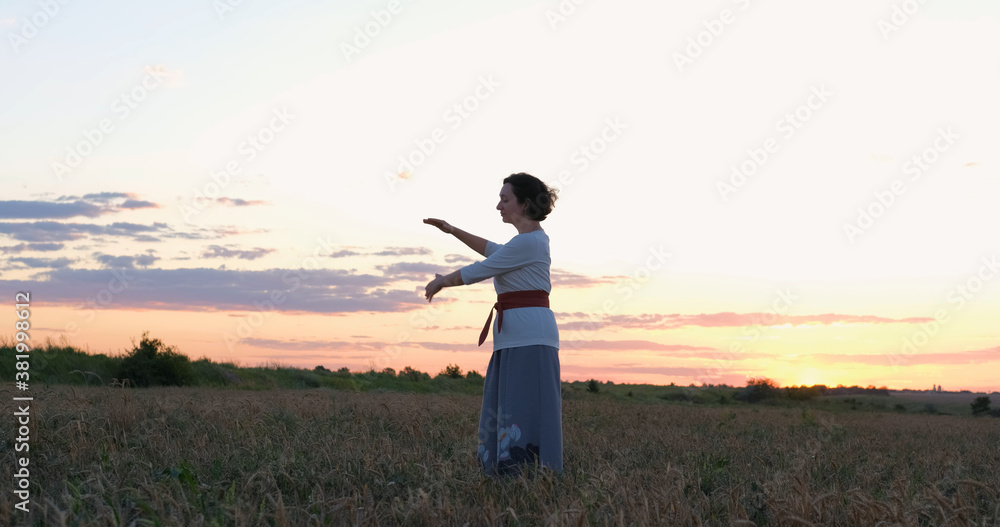 Female practicing qigong in summer fields with beautiful sunset on background Female practicing qigong in summer fields with beautiful sunset on background