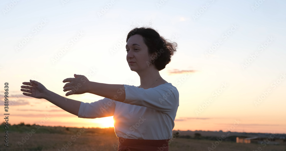 Female practicing qigong in summer fields with beautiful sunset on background Female practicing qigong in summer fields with beautiful sunset on background