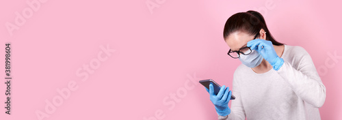 Portrait of a brunette girl with eyeglasses in a medical mask and blue rubber gloves using cellphone, copy space template, banner.