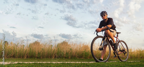 Cyclist sits on a gravel bicycle in a field at the golden hour. Active lifestyle concept. Copy space.