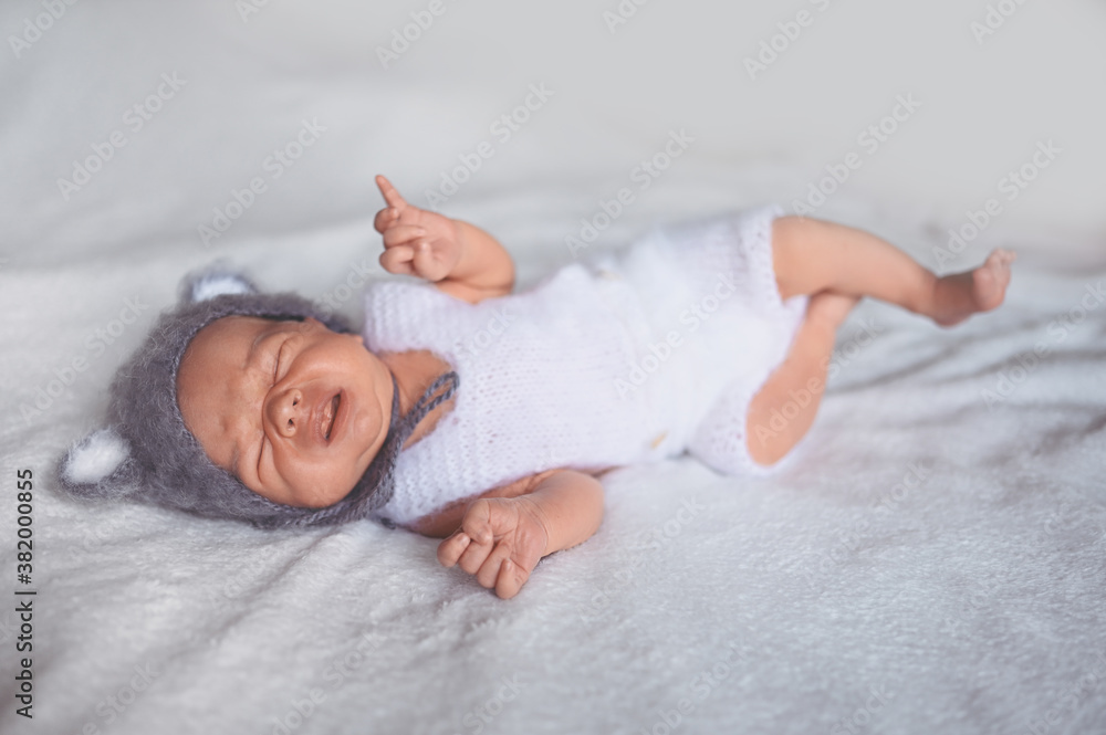 Cute crying newborn little baby boy sleeping in crib in a knitted suit with ears. Baby goods packaging template. Healthy child, concept of hospital and happy motherhood. Infant baby. Nursery Cute crying newborn little baby boy sleeping in crib in a knitted suit with ears. Baby goods packaging template. Healthy child, concept of hospital and happy motherhood. Infant baby. Nursery