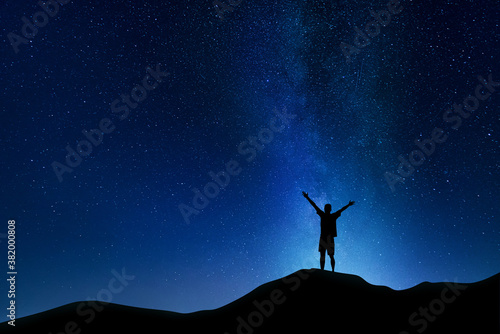 Beautiful night landscape of the milky way in the starry sky and silhouette of a young guy with his hands up.