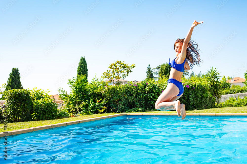 Beautiful girl jump in mid air into the swimming pool view from side scream and smile with hands up in funny pose