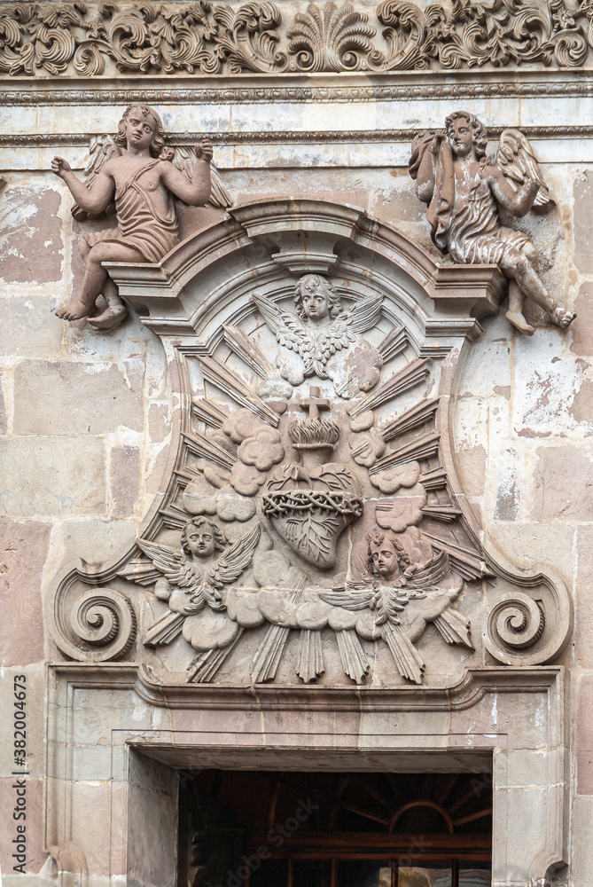 Quito, Ecuador - December 2, 2008: Historic downtown. Closeup of statue of mural with heart, angels and cross on Brown stone entrance facade to La Compania Church of the Jesuits.
