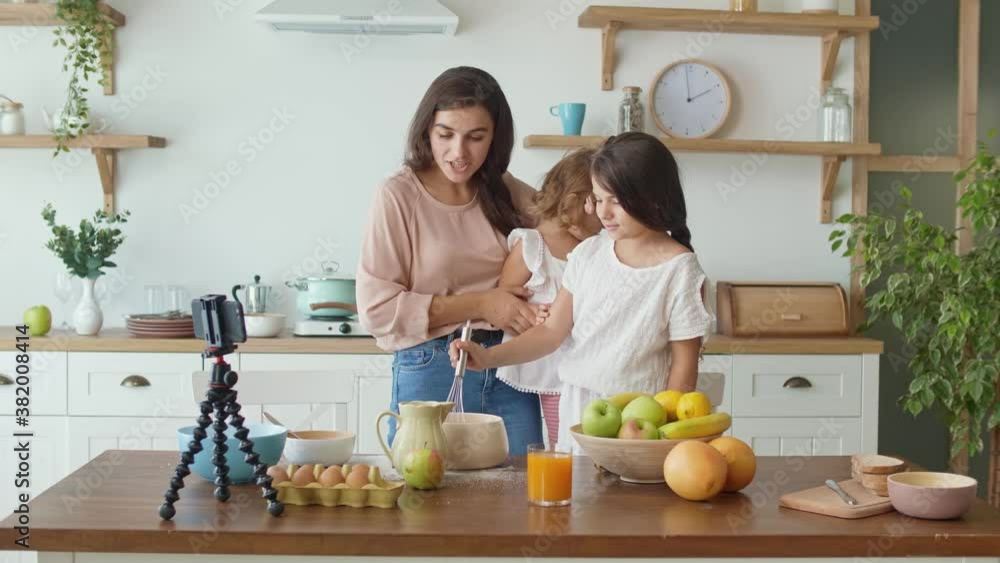 A Pretty Mother With a Two Daughters Shooting a Blog About Cooking. Video Blog of Healthy Food. A Mother With Children Streaming Online Video Vlog. Lovely Mother Teaching Her Daughters to Cook. A Pretty Mother With a Two Daughters Shooting a Blog About Cooking. Video Blog of Healthy Food. A Mother With Children Streaming Online Video Vlog. Lovely Mother Teaching Her Daughters to Cook.