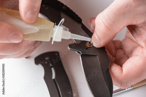 Fotografia Close-up on repairman's hands lubricating a pocket knife with household oil