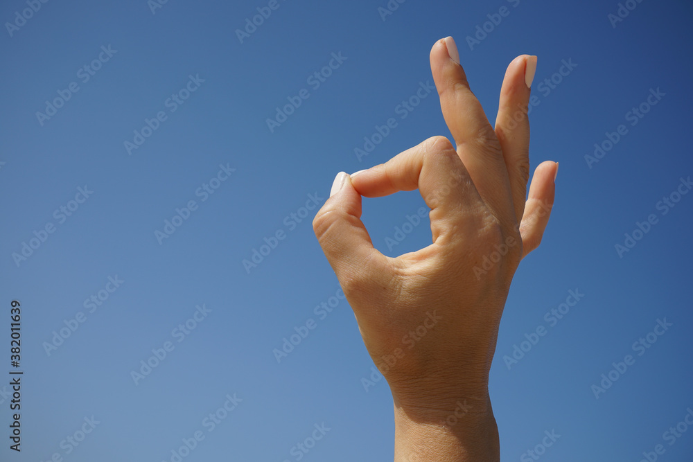 beautiful female hand demonstrates the symbol OK okay against the background of a clear blue sky on a clear sunny day beautiful female hand demonstrates the symbol OK okay against the background of a clear blue sky on a clear sunny day