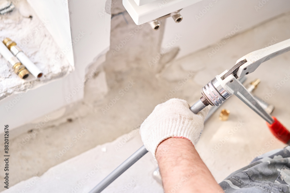 Plumber cuts the desired length of pipe with scissors tool. connection heating pipes to white Radiator in a new apartment under construction.