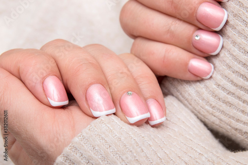 Women s hands with French manicure and rhinestones on rectangular nails on the background of a sweater