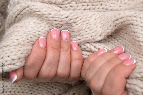 Women's hands with French manicure and rhinestones on rectangular nails on the background of a sweater. Winter concept