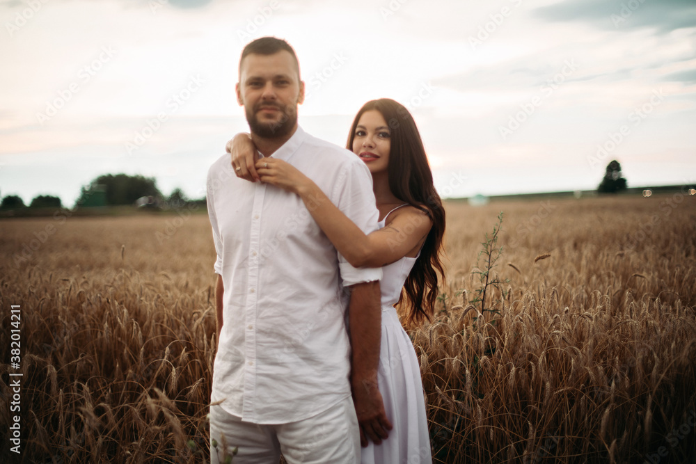 Stock photo portrait of bearded boyfriend hugging his gorgeous girlfriend both in white clothes hugging in wheat field. Beautiful wheat field in the background. Stock photo portrait of bearded boyfriend hugging his gorgeous girlfriend both in white clothes hugging in wheat field. Beautiful wheat field in the background.