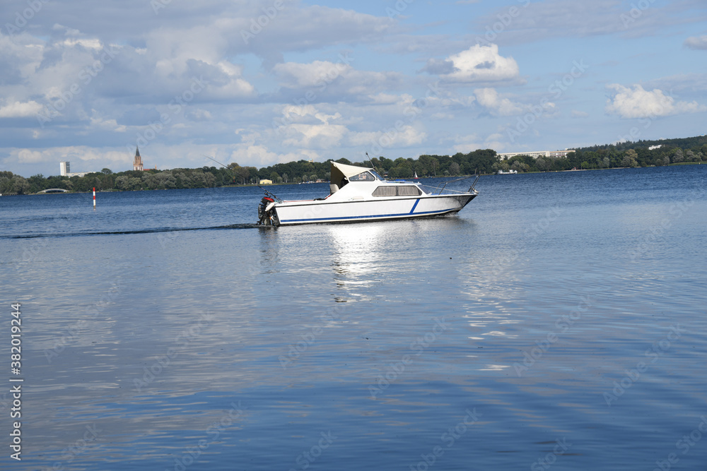 Obraz premium Ein Boot fährt auf dem Tollensesee vor den Toren Neubrandenburgs. Der See und die Stadt liegt im Gebiet der Mecklenburgischen-Seenplatte in Mecklenburg-Vorpommern. Viele Radwege 