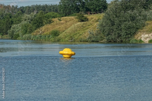 one large yellow plastic signal buoy in the blue water of the reservoir against the background of green vegetation and the sky