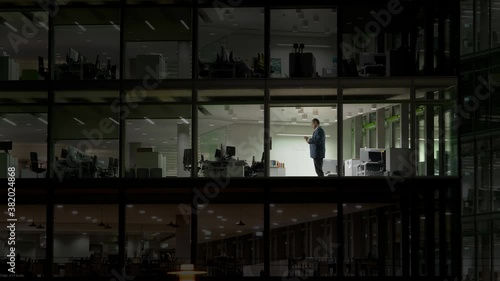 Man working late night in empty building with transparent glass window, tragic modern life without personal  happiness , work in corporate