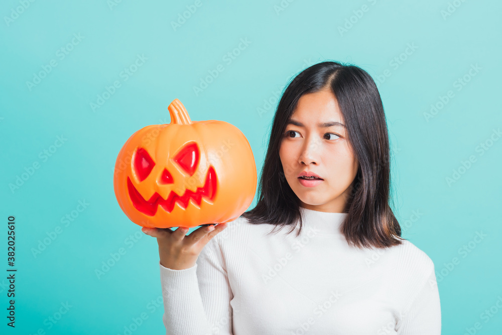 Portrait of Asian beautiful young woman holding orange model pumpkins, funny happy female with ghost pumpkins, studio shot isolated on blue background Portrait of Asian beautiful young woman holding orange model pumpkins, funny happy female with ghost pumpkins, studio shot isolated on blue background