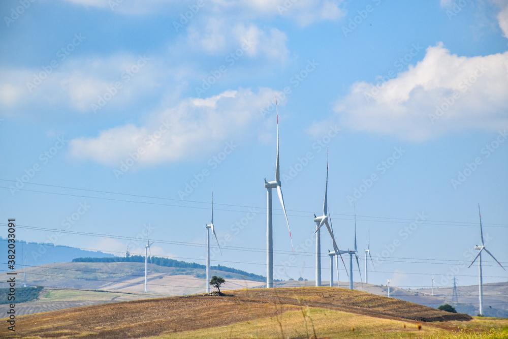 Barren hilly landscape with several wind turbines under a blue sky.