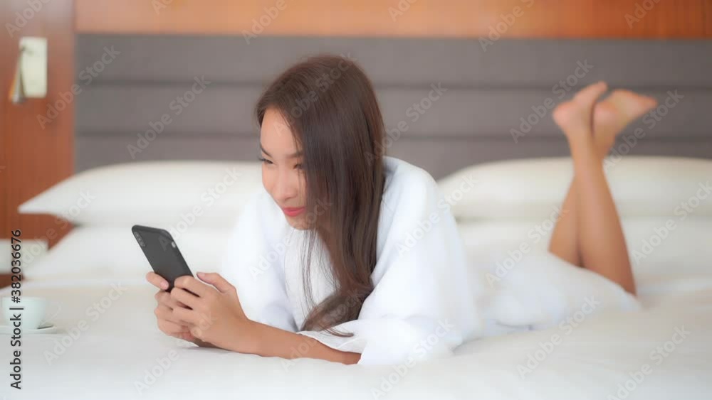 Relaxing in her hotel suite a pretty young woman, in a complimentary bathrobe, lies on the bed and texts friend and family. Relaxing in her hotel suite a pretty young woman, in a complimentary bathrobe, lies on the bed and texts friend and family.