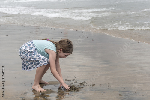 niña jugando con arena a la orilla del mar photo