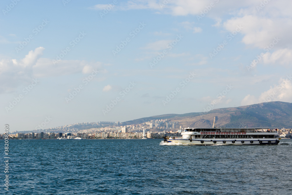 a ferry with passengers sails in the afternoon on the Aegean sea from the seaport of Izmir, surrounded by mountains, a city on the other side of the sea
