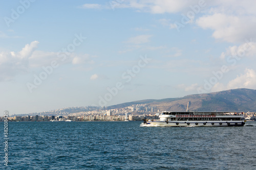 a ferry with passengers sails in the afternoon on the Aegean sea from the seaport of Izmir, surrounded by mountains, a city on the other side of the sea © Денис Кузнецов