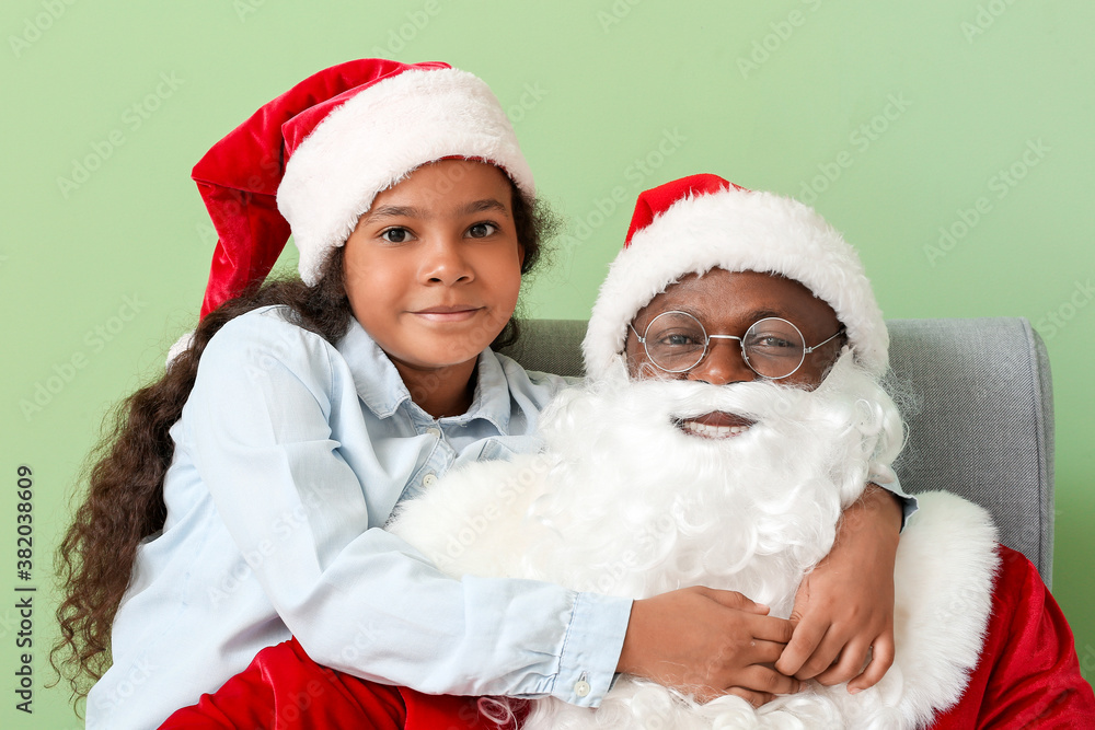 African-American Santa Claus with cute little girl on color background African-American Santa Claus with cute little girl on color background