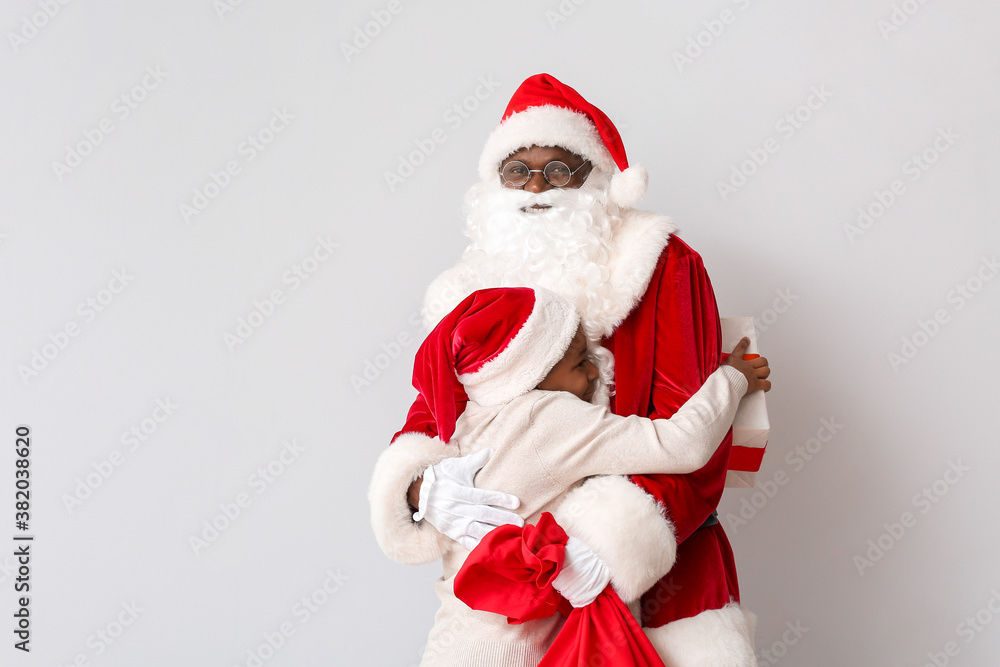 African-American Santa Claus hugging cute little boy on light background African-American Santa Claus hugging cute little boy on light background