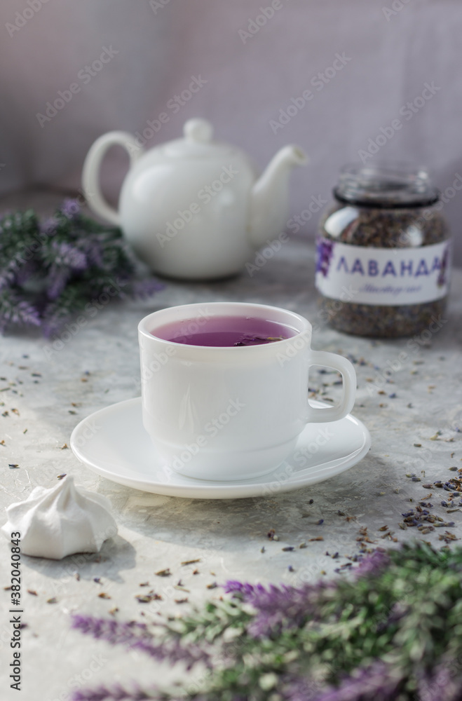 lavender tea in a white mug. Purple tea in a mug on a light background stands on the table next to lavender flowers. Dried lavender flowers are brewed in a Cup.