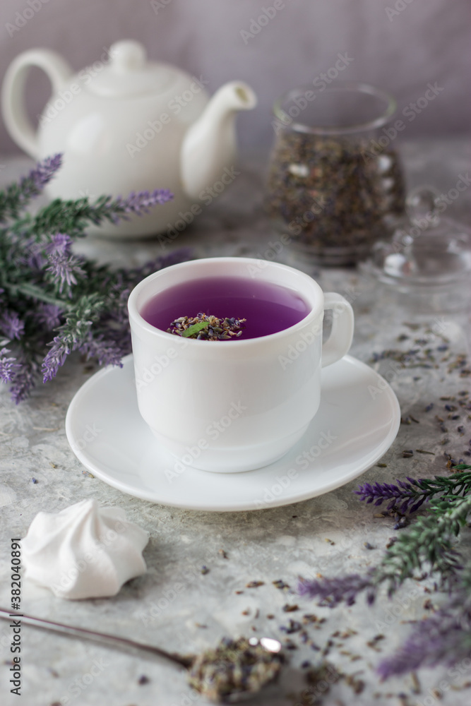 lavender tea in a white mug. Purple tea in a mug on a light background stands on the table next to lavender flowers. Dried lavender flowers are brewed in a Cup. lavender tea in a white mug. Purple tea in a mug on a light background stands on the table next to lavender flowers. Dried lavender flowers are brewed in a Cup.