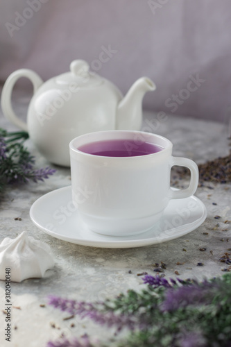 lavender tea in a white mug. Purple tea in a mug on a light background stands on the table next to lavender flowers. Dried lavender flowers are brewed in a Cup.