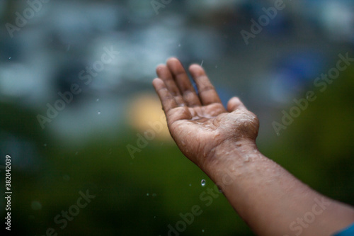 A palm catching raindrops out of the window